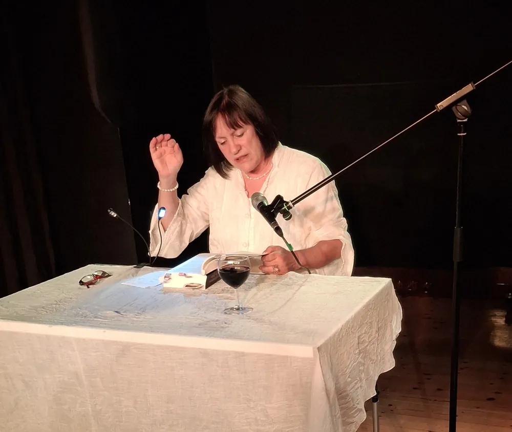 Kristina Rössler-Lehnhoff liest bei der Sololesung in Berlin-Pankow an einem Tisch mit Mikrofon und aufgeschlagenem Buch
